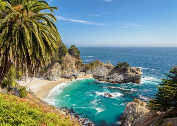 Turquoise water meets the sand at the edge of a cliff in Big Sur, California