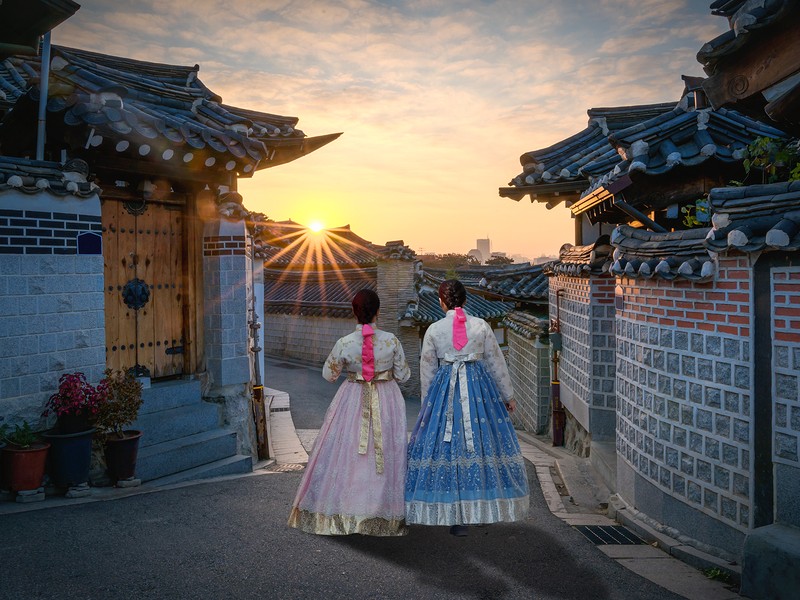 Back of two women wearing hanbok walking through the traditional style houses of Bukchon Hanok Village in Seoul South Korea.