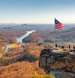 Mountaintop view of fall foliage with river and rock jutting out with American flag