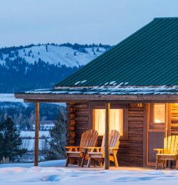 Log cabin with green roof surrounded by snowy landscape and mountains