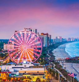 aerial view down the coast with ocean, beach, and boardwalk with ferris wheel in view at sunset