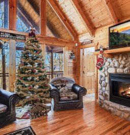 Living room with wood walls and stone fireplace decorated with Christmas stockings and Christmas tree in between two chairs