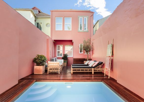 Pastel pink villa with pool in front and square building behind