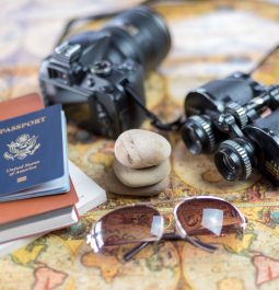 A camera, binoculars, sunglasses, passport and small travel book are spread out on a map.