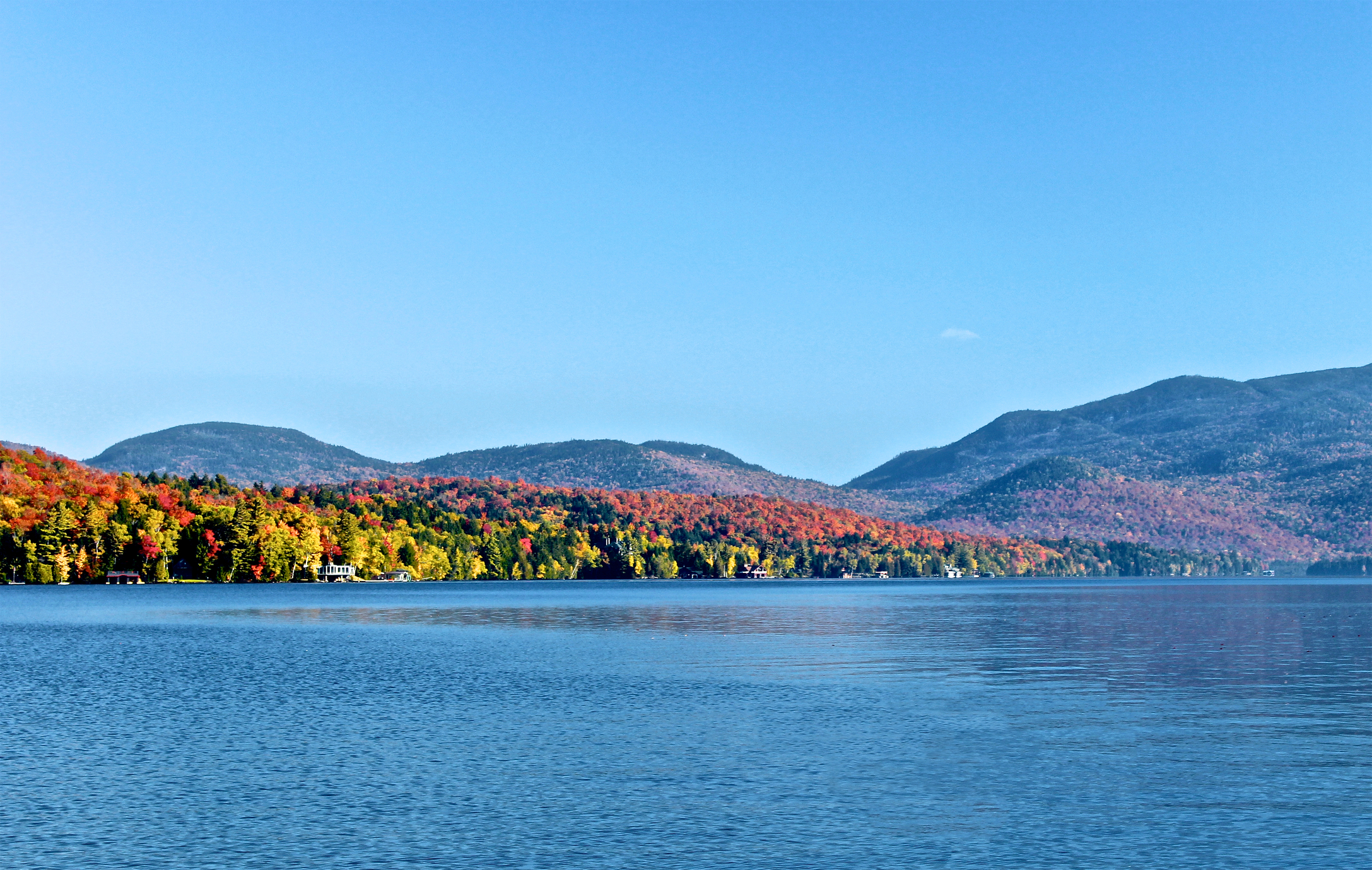 Beautiful colorful autumn leaves dot the fall trees surrounding blue lake in Lake Placid 