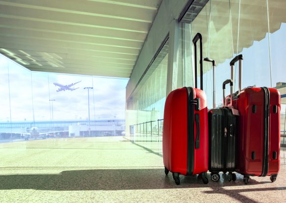 Three red suitcases sit in an empty terminal with floor to ceiling windows showing a plane taking off outside